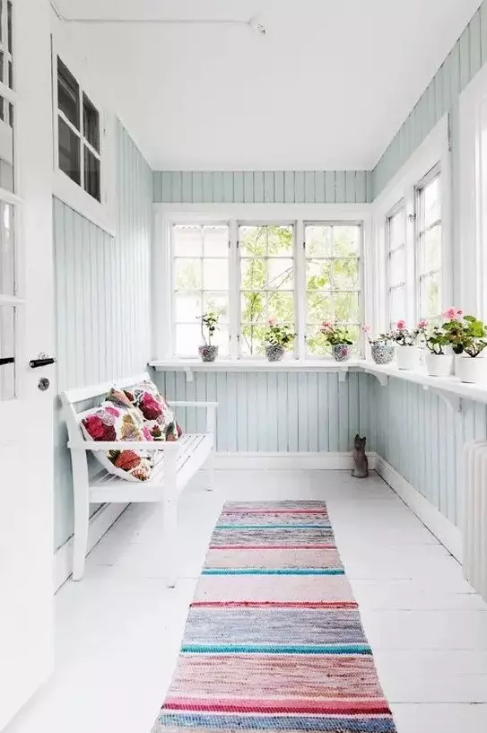 a small pastel sunroom in a light aqua shade, colorful textiles and a bench plus potted blooms
