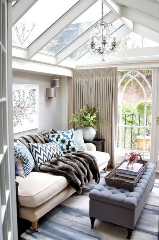 a small refined sunroom with elegant furniture, lots of pillows, a fir throw, a vintage chandelier and neutral curtains