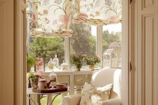 a small vintage sunroom with neutral furniture, floral printed shades and pillows, potted blooms and greenery