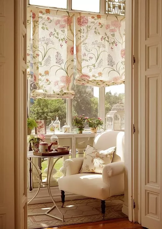 a small vintage sunroom with neutral furniture, floral printed shades and pillows, potted blooms and greenery