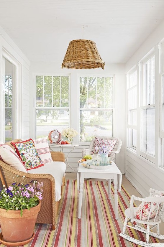 a small yet vibrant sunroom with neutral furniture, colorful printed textiles, a wicker pendant lamp and potted flowers