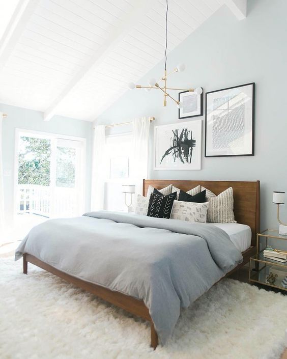a soothing modern bedroom with light blue walls, a stained bed with grey bedding and a mini gallery wall