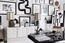 a stylish black and white home office with a polished black desk, a white storage unit, a monochromatic gallery wall and some table lamps