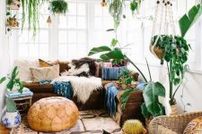a stylish boho sunroom with a brown sectional, colorful pillows, a rug, potted plants, a leather pouf and a statement cactus
