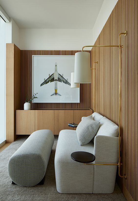 a stylish living room with wood slat walls, a grey loveseat and a footrest, a built in credenza and some wall lamps