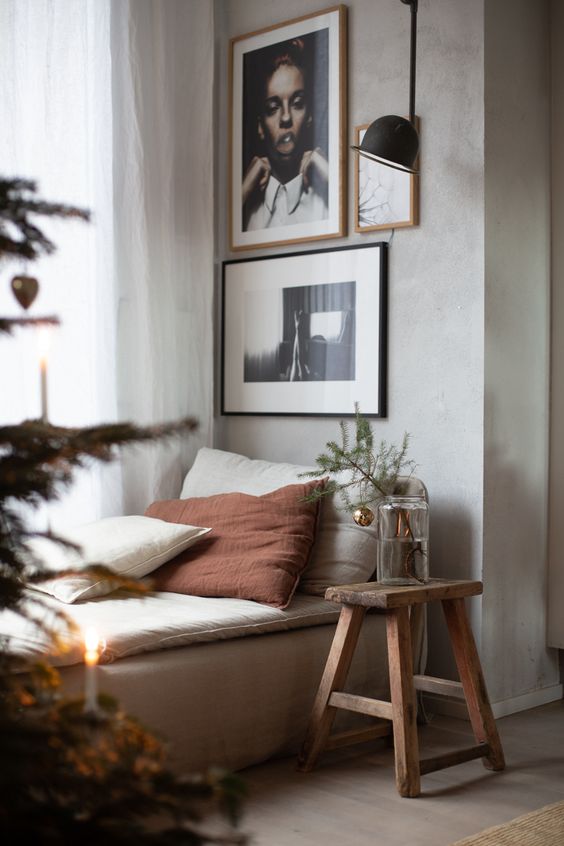 a stylish space with a daybed by the window, a small gallery wall, a black wall lamp, a wooden stool and a tree