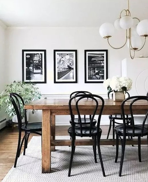 a stylish vintage dining room with a stained table and black chairs, a black and white mini gallery wall and potted plants and blooms
