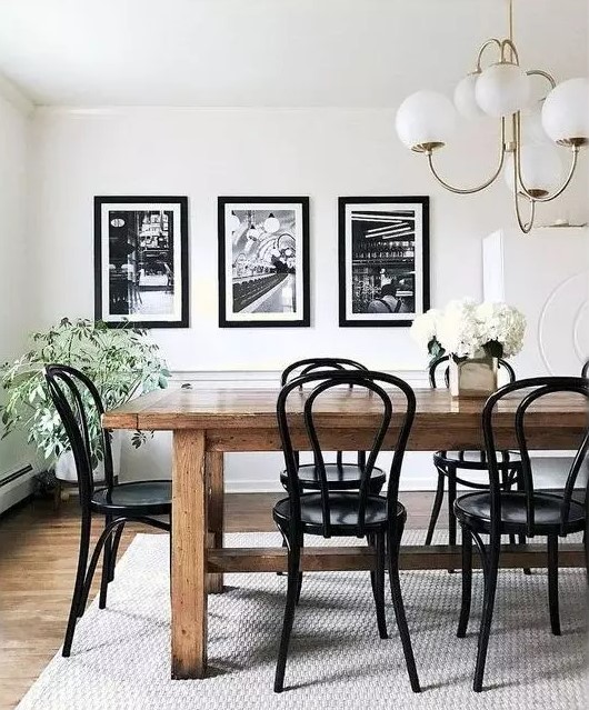 a stylish vintage dining room with a stained table and black chairs, a black and white mini gallery wall and potted plants and blooms