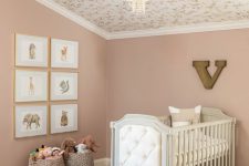 a subtle nursery with dusty pink walls, a floral wallpaper ceiling, a grey crib and some art and toys