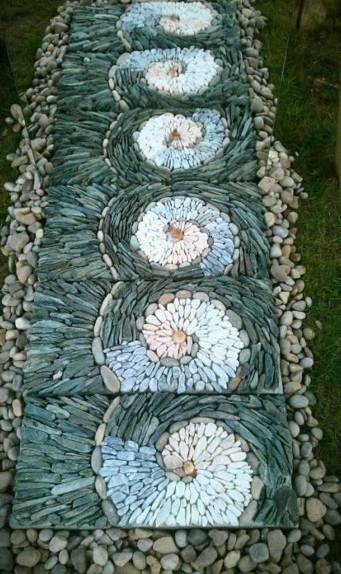 a unique garden pathway with neutral pebbles and tiles covered with grey, blue and white pebbles that are designed in swirls