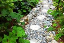 a very wild-looking garden path done with pebbles, large rocks and round tiles printed with leaves