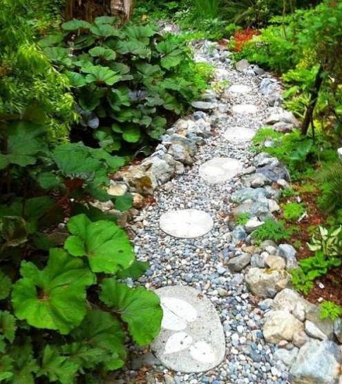a very wild looking garden path done with pebbles, large rocks and round tiles printed with leaves