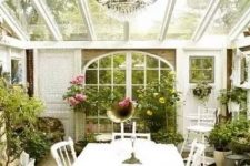 a vintage Scandinavian sunroom with lots of greenery and bold blooms, white vintage furniture, a crystal chandelier