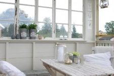 a vintage Scandinavian sunroom with shabby chic furniture, potted greenery, catchy chandelier, candle lanterns