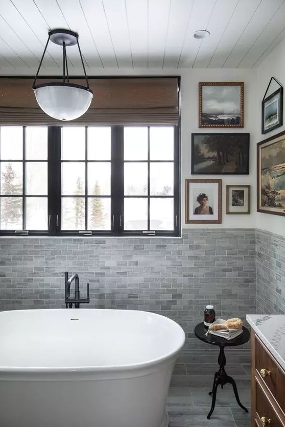 a vintage cottage bathroom with grey tiles, a vintage gallery wall, a modern soak tub and a black side table