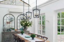 a vintage farmhouse sunroom as a dining space, with a shabby chic credenza, a stained table and vintage chairs, pendant lamps and elegant decor