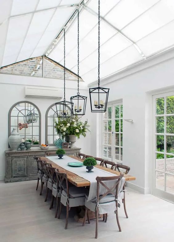 a vintage farmhouse sunroom as a dining space, with a shabby chic credenza, a stained table and vintage chairs, pendant lamps and elegant decor
