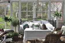a vintage farmhouse sunroom with a black forged daybed, a table and wicker chairs, greenery and a chic crystal chandelier