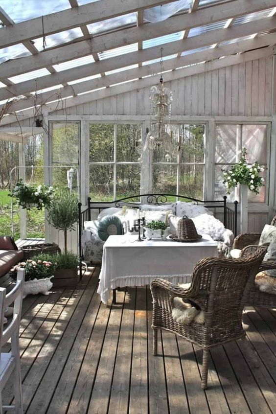a vintage farmhouse sunroom with a black forged daybed, a table and wicker chairs, greenery and a chic crystal chandelier