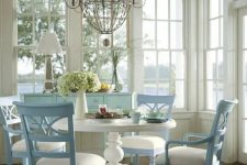 a vintage neutral and pastel sunroom with glazed walls, a white round table and powder blue chairs and an aqua sideboard plus bottles on display