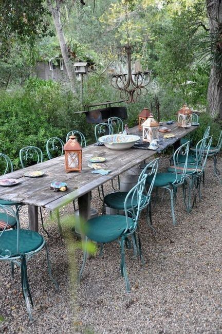a vintage outdoor dining space with a rustic shabby chic table, blue metal chairs with cushions and lanterns on the table