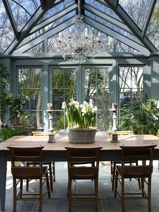 a vintage rustic sunroom in blue grey, with stained rustic furniture, potted greenery and blooms and a crystal chandelier