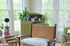 a vintage rustic sunroom with green and neutral wicker furniture, neutral textiles, potted greenery and a floral rug