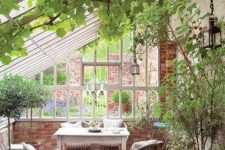 a vintage rustic sunroom with lots of greenery in pots and climbing ones, rattan and wooden furniture