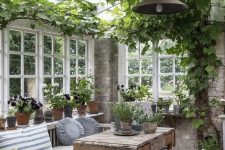 a vintage to shabby chic sunroom with neutral and stained furniture, potted greenery and blooms and vining greenery on the ceiling