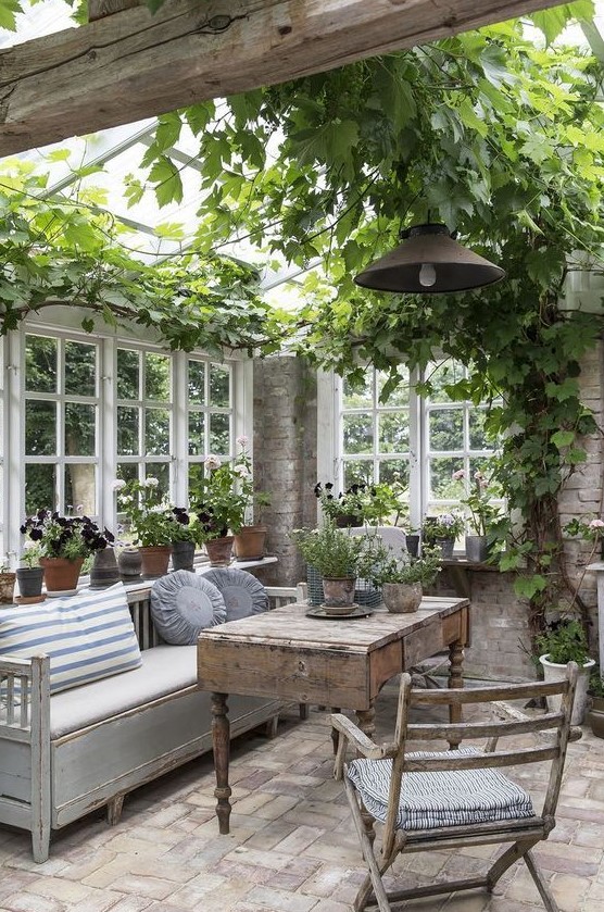 a vintage to shabby chic sunroom with neutral and stained furniture, potted greenery and blooms and vining greenery on the ceiling