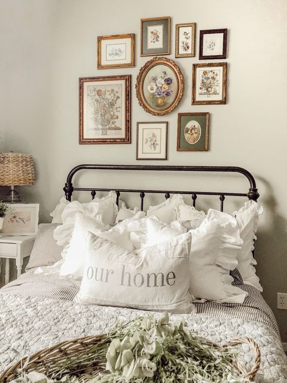 a vitnage farmhouse bedroom with a black forged bed with neutral bedding, a white nightstand with a woven lamp and a gallery wall of vintage artwork