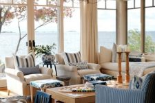 a welcoming coastal sunroom with series of windows, white and blue seating furniture, printed textiles, a vintage chandelier and some tables