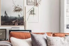 a welcoming living room with an amber leather sofa, neutral pillows, a mini gallery wall, a console table and some grasses
