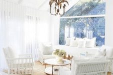 a white coastal sunroom with white rattan furniture, a sofa, a round table and a quirky chandelier is a lovely space
