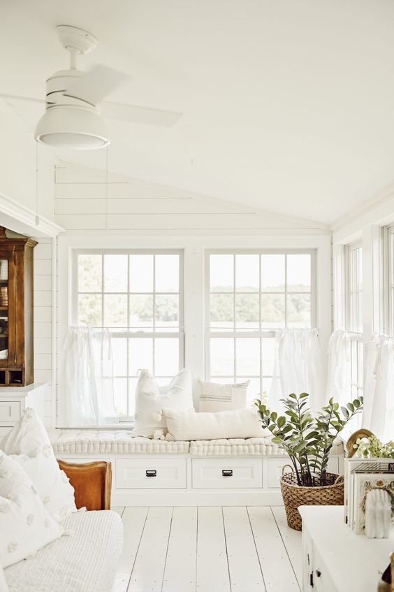 a white farmhouse sunroom with a built in daybed with storage drawers, a sofa, a dresser and a potted plant is amazing