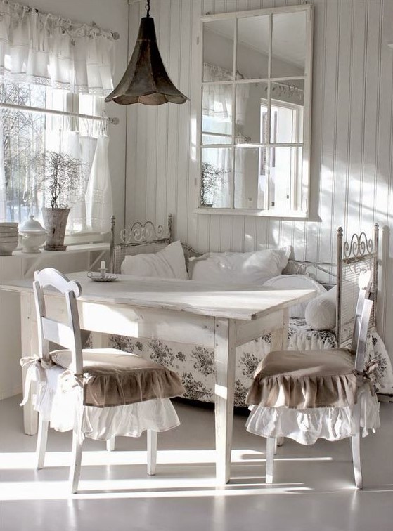 a white vintage sunroom with forged and wooden furniture, floral textiles, a metal lamp and a large mirror