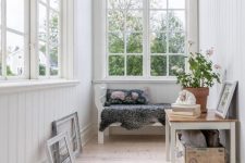 an airy small sunroom with a bench, a table with a crate and some artworks is a welcoming space