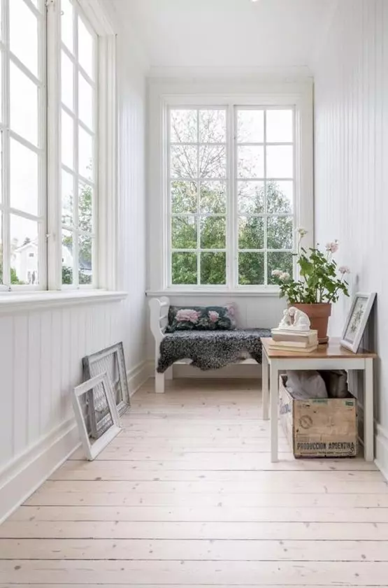 an airy small sunroom with a bench, a table with a crate and some artworks is a welcoming space