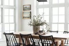an airy vintage dining room with a stained table, black chairs, a pendant lamp on chain and a mini gallery wall