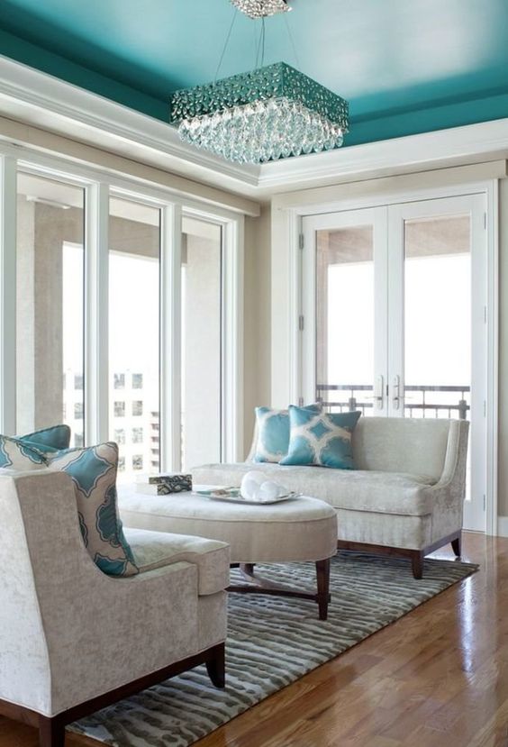 an elegant living room with neutral seating furniture, an emerald ceiling, an ottoman and a chic crystal chandelier