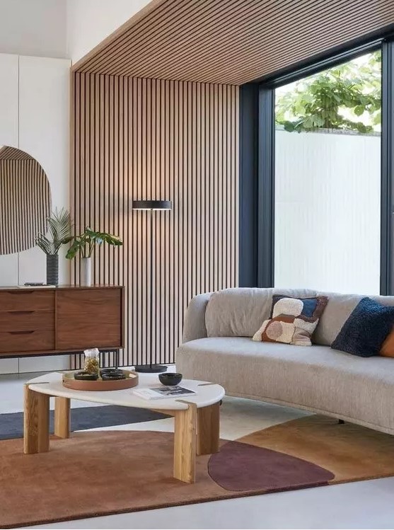 an elegant mid century modern living room with a wood slat accent wall and ceiling, a curved sofa, a printed rug, a stained credenza and a coffee tabl