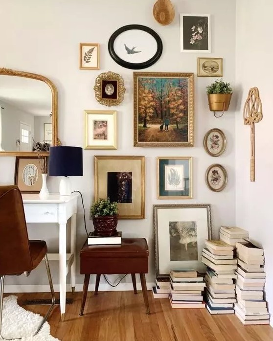 an elegant vintage home office with a white desk, a brown chair and a side table, a vintage gallery wall and a mirror plus stacks of books