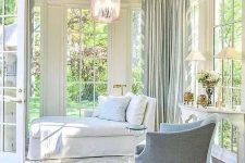 an elegant vintage sunroom with a white daybed and a light blue chair, a vintage table with lamps and a cool pendant lamp