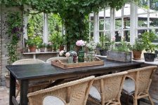 an enchanting vintage sunroom with a black table, wicker chairs, potted greenery and blooms and suspended lamps