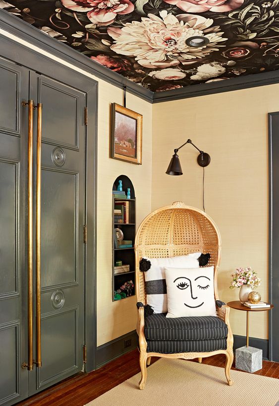 an exquisite nook with a niche with shelves, a dark floral wallpaper ceiling, a chic rattan chair, some blooms and art