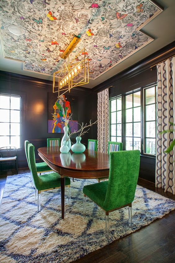an extra bold dining room with a colorful wallpaper ceiling, a stained table, bold green chairs, printed textiles and artwork