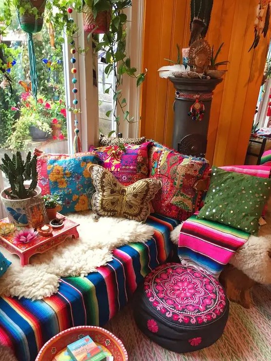 an extra colorful boho sunroom with a bright sectional, colorful pillows, blakets, ottomans, potted plants and pompoms
