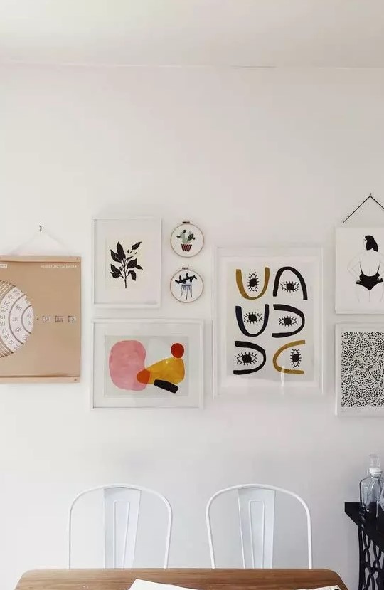 an eye-catchy gallery wall with white and blonde wood frames, with bold graphic artworks is chic and cool