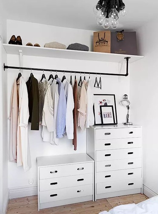 a small makeshift closet with dressers, a holder for hangers, an open shelf right in the bedroom