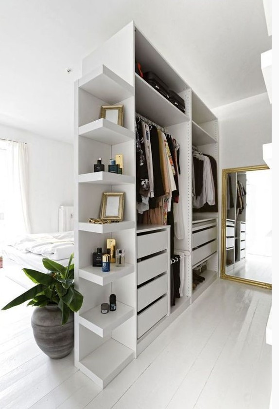 a small open closet in white with shelves, holders and drawers doubles as a space divider